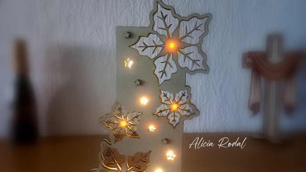 Pieza decorativa navideña que aúna arte, creatividad y funcionalidad: una escultura en madera con corte láser, compuesta por dos partes verticales encajadas perpendicularmente sobre una base, con luces LED en su interior.