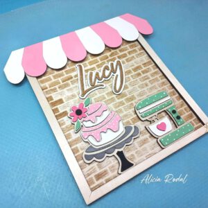 Hoy quiero compartir contigo el proceso detrás de una de mis creaciones más especiales: un cuadro de madera diseñado, cortado, grabado y pintado a mano, que representa una pequeña tienda u obrador de repostería. Esta pieza, pensada como regalo personalizado, forma parte del catálogo de mi tienda de arte y regalos personalizados, Alicia Rodal.
